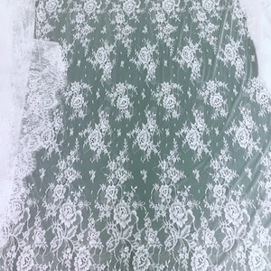 May include: White floral lace fabric with a delicate pattern. The lace has a scalloped edge and is sheer and lightweight.