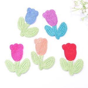 Op de afbeelding: Vijf gehaakte tulp applicaties in verschillende kleuren. Elke bloem heeft een andere kleur: blauw, roze, paars, perzik en rood. De groene bladeren en stelen zorgen voor contrast. Deze handgemaakte applicaties zijn geschikt voor knutselprojecten.