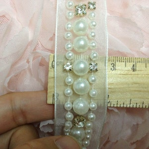 May include: White pearl and rhinestone trim with a sheer fabric backing. The trim is approximately 3 inches long.
