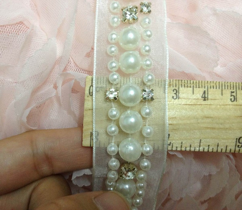 May include: White pearl and rhinestone trim with a sheer fabric backing. The trim is approximately 3 inches long.