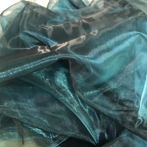 May include: Teal iridescent sheer fabric with a shimmery finish. The fabric is folded and draped, showing its texture and drape.