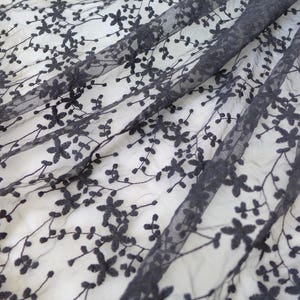 K&ouml;nnte beinhalten: Schwarzer Blumenspitze Stoff mit einem zarten Muster aus kleinen Bl&uuml;ten und Bl&auml;ttern. Die Spitze ist durchsichtig und hat eine weiche, flie&szlig;ende Textur.