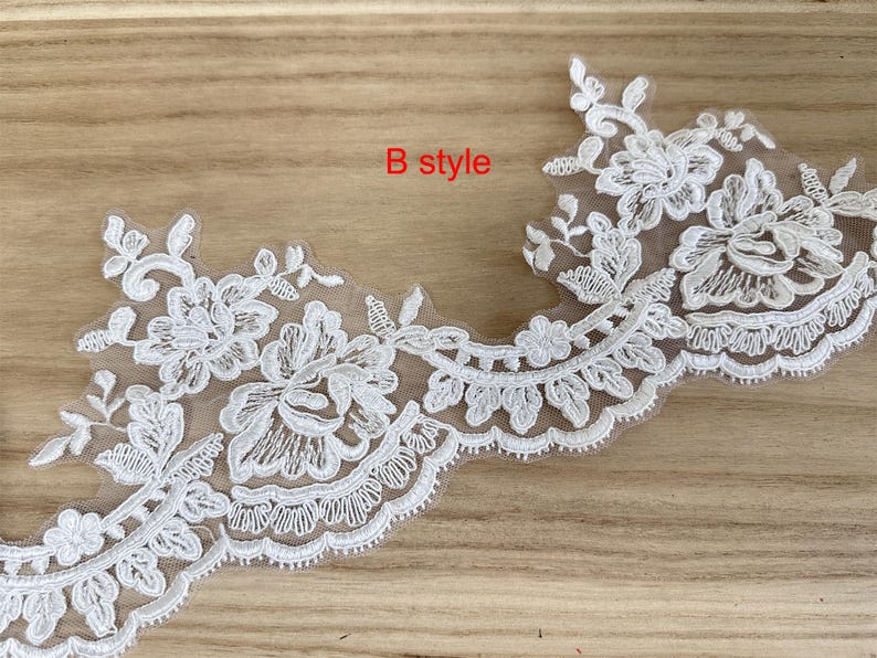 May include: White floral lace trim with a scalloped edge. The lace features detailed embroidered flowers and leaves. The text "B style" is in red. Ideal for embellishing garments or crafts.