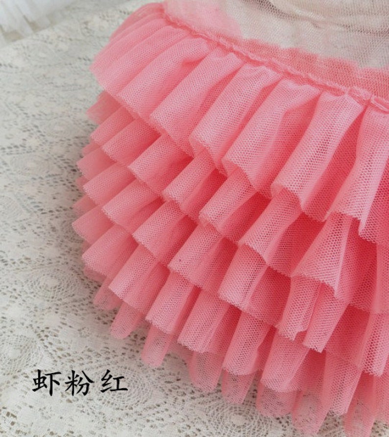 May include: Pink ruffled tulle trim with multiple layers. The trim is soft and delicate, perfect for adding a touch of femininity to any project.