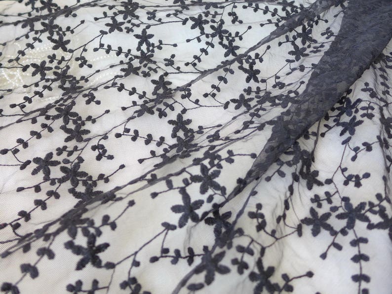 K&ouml;nnte beinhalten: Schwarzer Blumenspitzenstoff mit einem zarten Muster aus kleinen Bl&uuml;ten und Bl&auml;ttern. Die Spitze ist durchsichtig und hat eine weiche, flie&szlig;ende Textur.