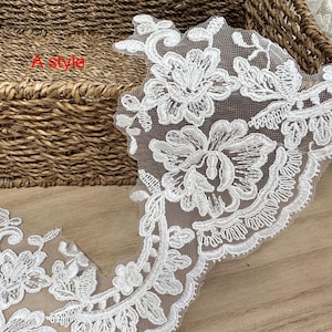 May include: White floral lace trim with a delicate, openwork design. The lace features detailed flower and leaf patterns, ideal for embellishing garments or crafts. The text "A style" is visible in the image.