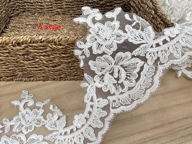 May include: White floral lace trim with a delicate, openwork design. The lace features detailed flower and leaf patterns, ideal for embellishing garments or crafts. The text "A style" is visible in the image.