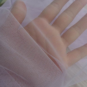 May include: A close-up of a pale lavender sheer fabric with a fine mesh texture. The fabric is soft and delicate, with a slightly iridescent sheen.