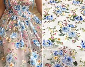 May include: White tulle fabric with embroidered blue and pink flowers. The fabric is sheer and delicate, with a floral pattern that is both elegant and whimsical.