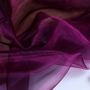 May include: A close-up of a sheer, purple fabric with a slight sheen. The fabric is draped and folded, creating soft, flowing lines.