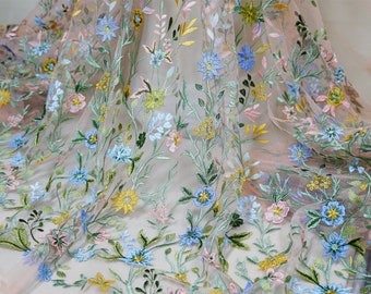 May include: Pale pink tulle fabric with embroidered floral designs in shades of blue, yellow, and pink. The flowers are scattered throughout the fabric, creating a delicate and romantic look.
