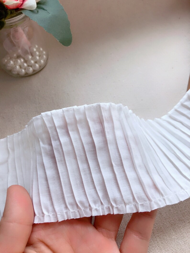 K&ouml;nnte beinhalten: Wei&szlig;er gefalteter Stoffbesatz mit einem gen&auml;hten Rand. Der Besatz ist in der Mitte gefaltet und zeigt die Falten auf beiden Seiten.