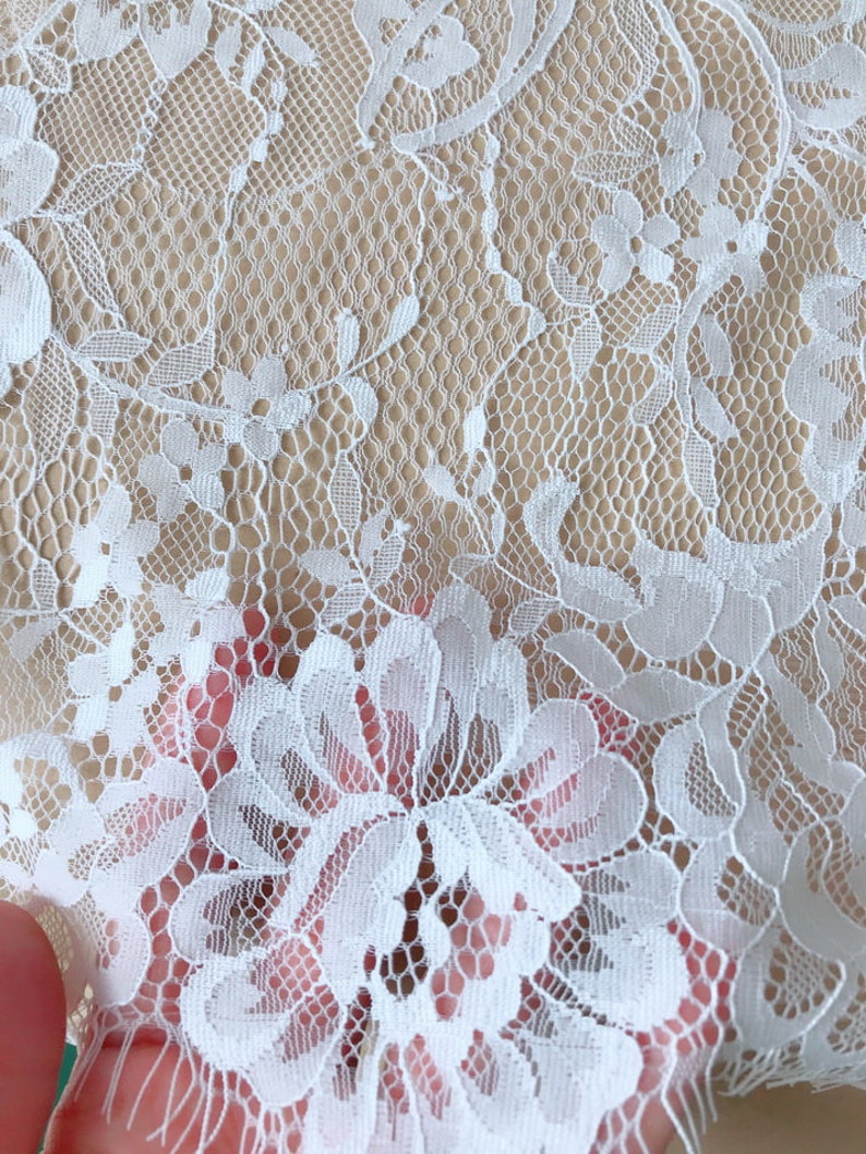 May include: White lace fabric with a delicate floral pattern. The lace has a fine mesh texture and is soft to the touch.