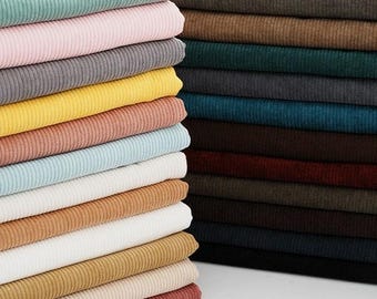 May include: Two stacks of folded corduroy fabric in a variety of colors. The left stack features lighter shades including mint, pink, gray, yellow, peach, and light blue. The right stack contains darker tones like brown, teal, burgundy, and black.