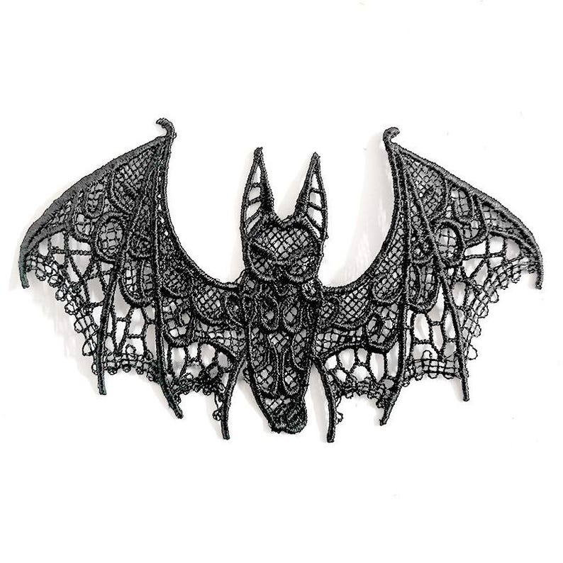 May include: A black lace bat with detailed openwork patterns. The bat's wings are spread wide. The decorative bat is likely for Halloween or gothic-themed decor. The lace has a textured appearance.