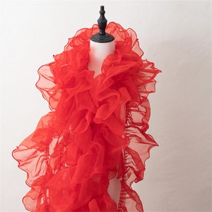 May include: A red tulle scarf with a ruffled design. The scarf is draped over a mannequin.