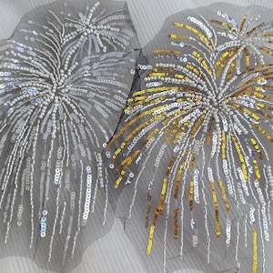 May include: Two decorative appliques with a fireworks design. One is silver and white, the other gold and white. Both are made of sequins and beads on a black mesh backing. The appliques are ideal for embellishing clothing or accessories.