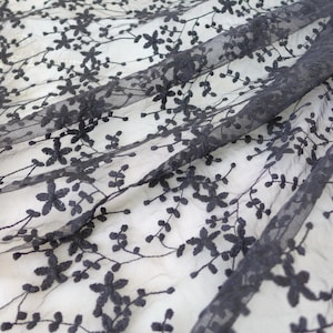 K&ouml;nnte beinhalten: Schwarzer Blumenspitzenstoff mit einem zarten Muster aus kleinen Bl&uuml;ten und Bl&auml;ttern. Die Spitze ist durchsichtig und hat eine weiche, flie&szlig;ende Textur.