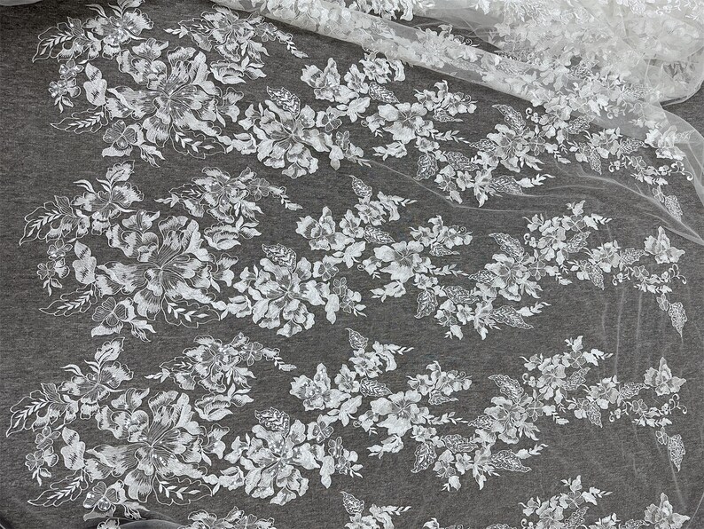 May include: White floral lace fabric with a delicate pattern of flowers and leaves. The lace is on a sheer mesh background.