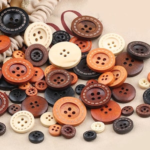 Puede incluir: Una colección de botones de madera de varios tamaños y colores, que van desde el marrón claro hasta el naranja y el crema. Algunos botones tienen costuras decorativas. Están esparcidos sobre un fondo neutro y tienen cuatro agujeros.