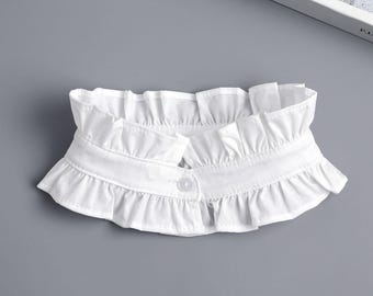 May include: A white detachable collar featuring a double-layered ruffled trim along the top and bottom edges. The collar is constructed from a smooth fabric and includes a single clear button closure at the center front to secure the garment.