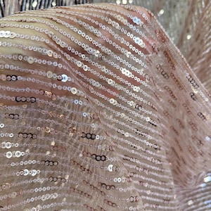 Puede incluir: Primer plano de una tela rosa claro transparente adornada con filas de pequeñas lentejuelas brillantes. Las lentejuelas están dispuestas en líneas diagonales, creando un efecto texturizado y brillante. La tela es ligeramente translúcida.