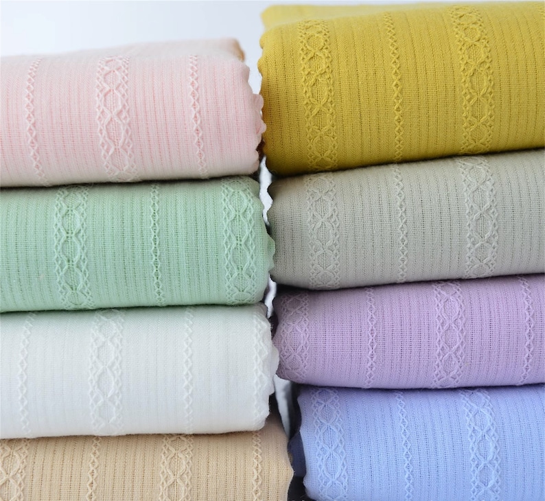 May include: A stack of six fabric swatches in various colors, including pink, green, white, beige, purple, and blue. Each swatch has a delicate lace trim and a striped pattern.