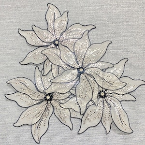 May include: Three white flower-shaped fabric appliques with silver sequins and black outlines.