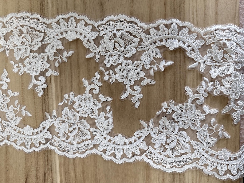 May include: White floral lace trim with a scalloped edge. The lace features detailed floral and leaf patterns. The trim is ideal for sewing, crafting, or adding a delicate touch to garments or home decor projects.
