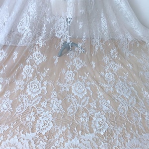 May include: White floral lace fabric with a delicate pattern. The lace has a scalloped edge and is sheer.