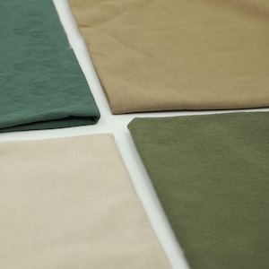 May include: Four fabric swatches in shades of green, tan, and beige are arranged in a square. The fabrics have a textured appearance, suggesting a linen or similar material. The colors range from a deep forest green to a light, creamy beige.