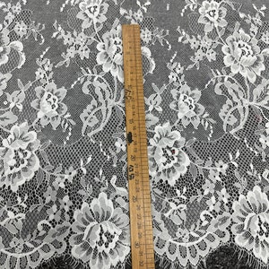 May include: White floral lace fabric with a delicate pattern. The fabric is shown next to a ruler measuring 36 inches.