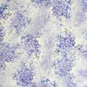 May include: A fabric or paper surface featuring a repeating pattern of clusters of small, light purple and violet flowers. The floral design is set against a textured, off-white background, creating a soft, layered appearance with varied shades.