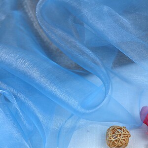 May include: Light blue sheer fabric with a soft, flowing texture. The fabric is draped over a white surface.