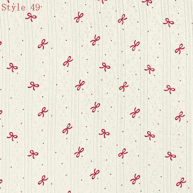 May include: Off-white fabric featuring a repeating pattern of small red bows and tiny red dots. The material has a vertical ribbed texture with subtle eyelet detailing between the ribs. The text Style 49 is printed in the top left corner.