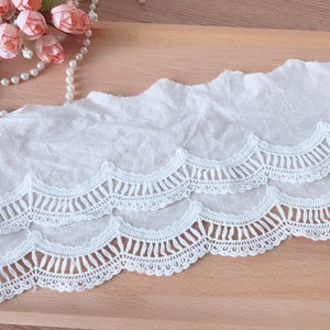 May include: White cotton lace trim with a scalloped edge. The lace has a delicate, intricate design with multiple layers.