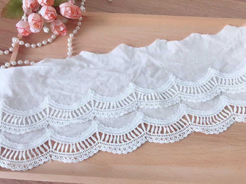 May include: White cotton lace trim with a scalloped edge. The lace has a delicate, intricate design with multiple layers.