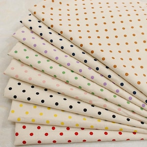 May include: A stack of folded fabric pieces, each featuring a cream-colored base with a repeating pattern of polka dots in various colors including brown, dark blue, purple, green, light pink, black, yellow, and red arranged in neat rows.