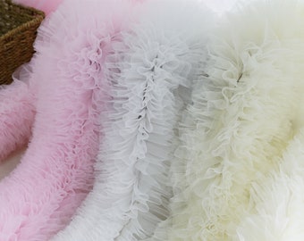 Può includere: Tre rotoli di tessuto di tulle arricciato in rosa, bianco e crema. Il tessuto è morbido e delicato, con una texture arricciata a strati.