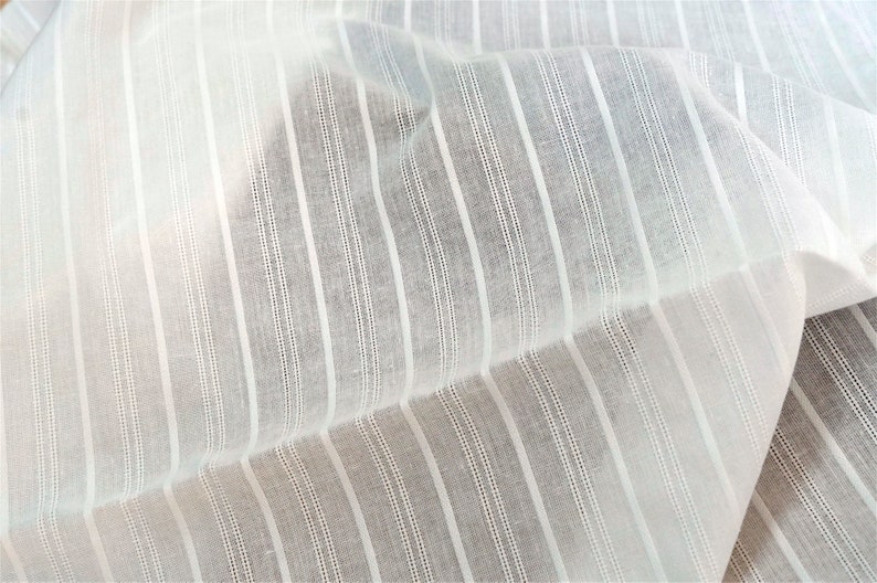 May include: White cotton fabric with thin, vertical stripes. The fabric is sheer and has a slightly textured surface.