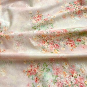 May include: A close-up of a fabric with a floral pattern. The fabric is a light pink color with a repeating pattern of pink and peach roses, with green leaves. The fabric is folded, creating shadows and depth.