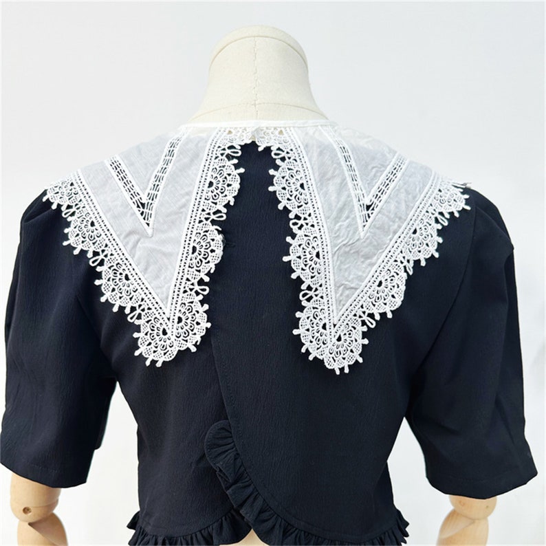 Puede incluir: Blusa negra con cuello de encaje blanco. El cuello presenta intrincados detalles de encaje en los bordes. La blusa tiene mangas cortas y un dobladillo con volantes, agregando un toque de elegancia al dise&ntilde;o.