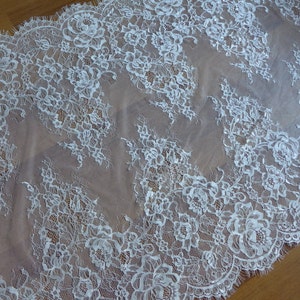 May include: White lace fabric with a delicate floral pattern. The lace has a scalloped edge and is sheer.