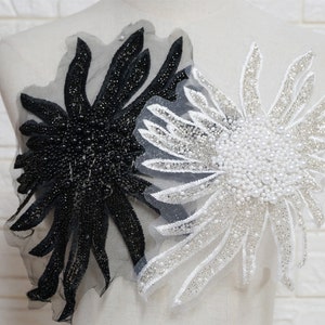 May include: Two decorative floral appliques. One is black with black beads and sequins, the other is white with white beads and silver sequins. Both are on a sheer, gray backing.