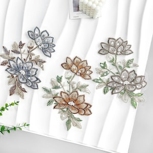 Puede incluir: Tres apliques florales bordados en tonos azules, marrones y grises, con detalles de lentejuelas y abalorios. Cada aplique presenta diseños detallados de flores y hojas, ideales para embellecer prendas o manualidades.