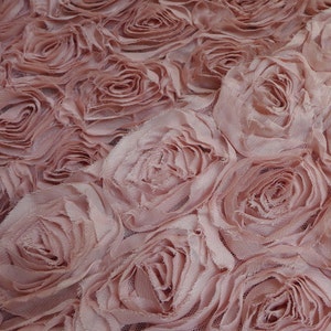 Puede incluir: Primer plano de una tela con un patrón repetido de rosas rosas claras tridimensionales. Las rosas están hechas de pétalos de tela en capas, creando un diseño floral texturizado. El fondo es una malla fina, que añade profundidad.