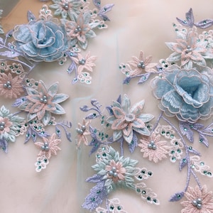May include: Delicate floral lace fabric featuring 3D flowers in shades of blue, pink, and green. The flowers are embellished with pearls and rhinestones.