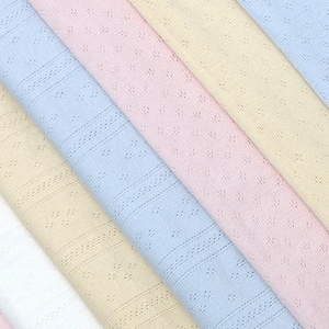 May include: A close-up shot of pastel-coloured fabrics in pink, blue, yellow, and white. The textiles feature a delicate openwork design with small, evenly spaced holes and subtle striped patterns, suggesting a breathable material.