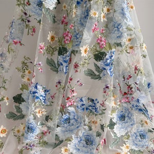Puede incluir: Tela blanca transparente con un patr&oacute;n floral. Las flores son azules, rosas y blancas. La tela es delicada y tiene una textura suave.