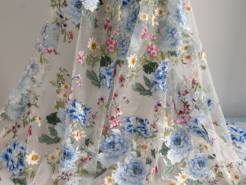 Puede incluir: Tela blanca transparente con un patr&oacute;n floral. Las flores son azules, rosas y blancas. La tela es delicada y tiene una textura suave.